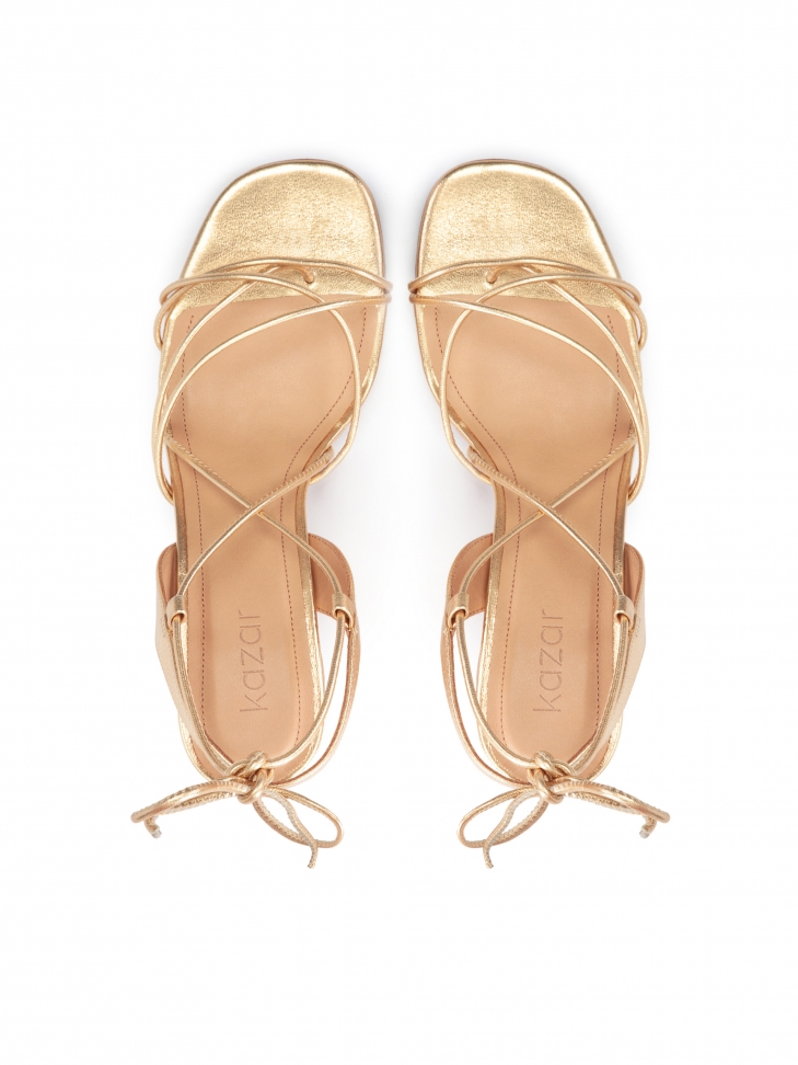 Złote sandały na słupku wiązane wokół łydki